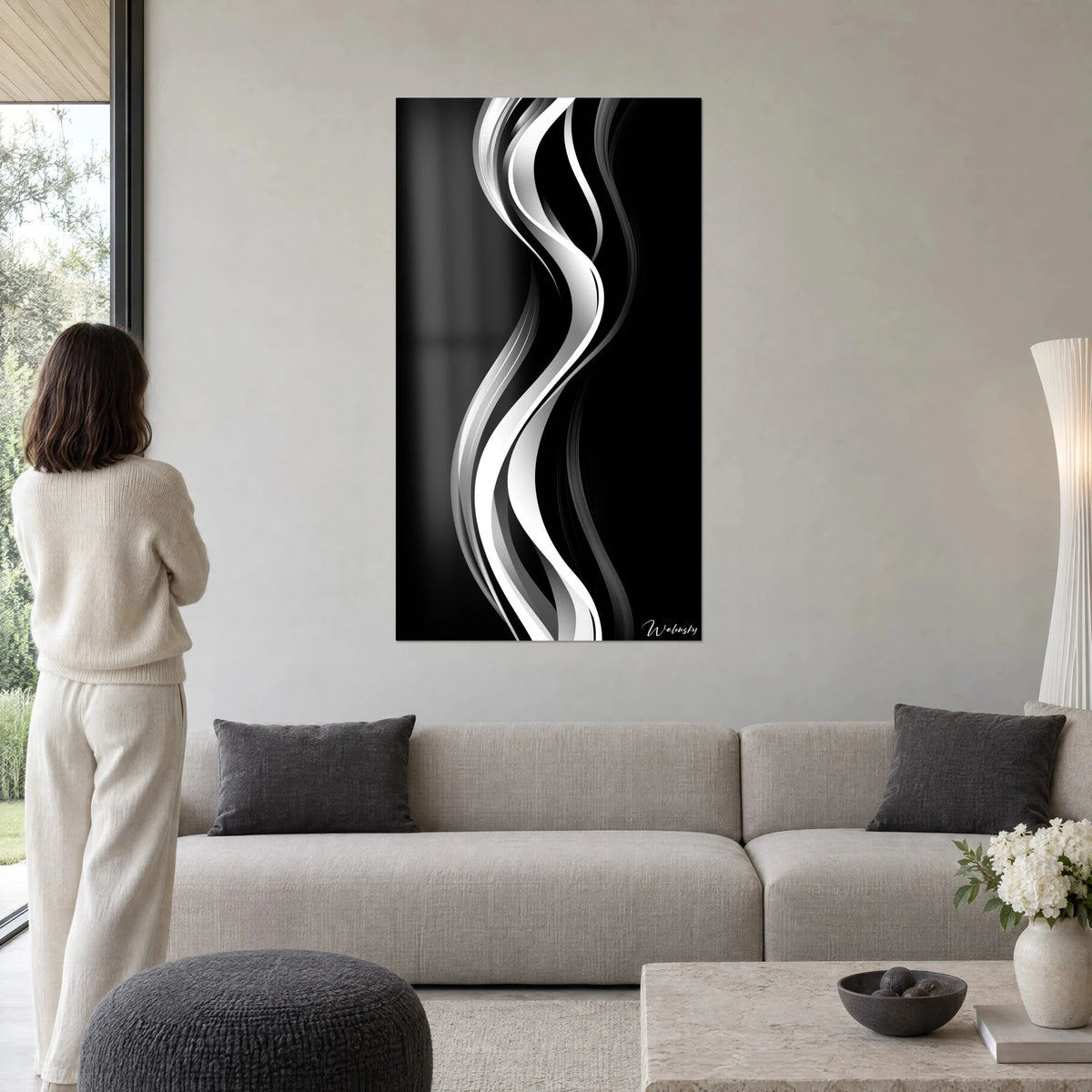Schilderij golvende linten in wit en grijs op zwarte achtergrond, vrouw van achteren vooraan, boven een bank in een lichte woonkamer