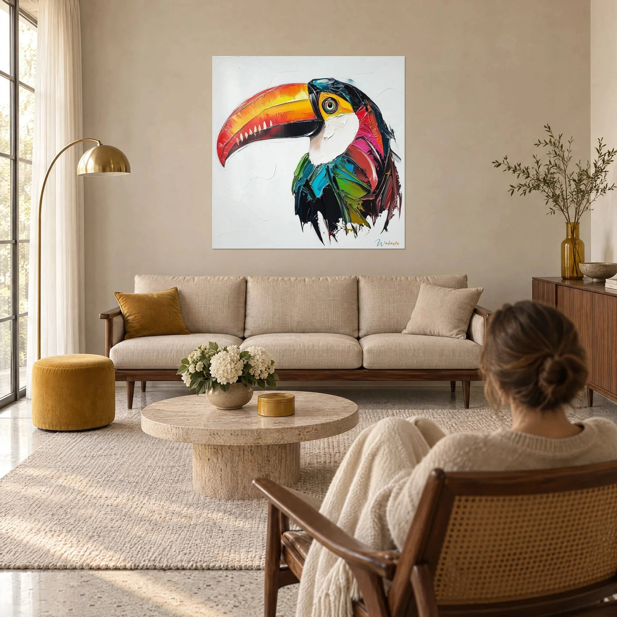 Wall art toucan with orange and yellow beak in palette-knife strokes, green and pink plumage on a white background, above a sofa in a bright living room