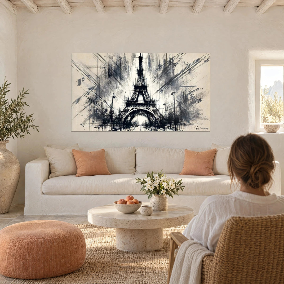 Tableau Tour Eiffel en encre noire et gris charbon sur fond crème, une femme de dos au-dessus d'un canapé dans un salon lumineux