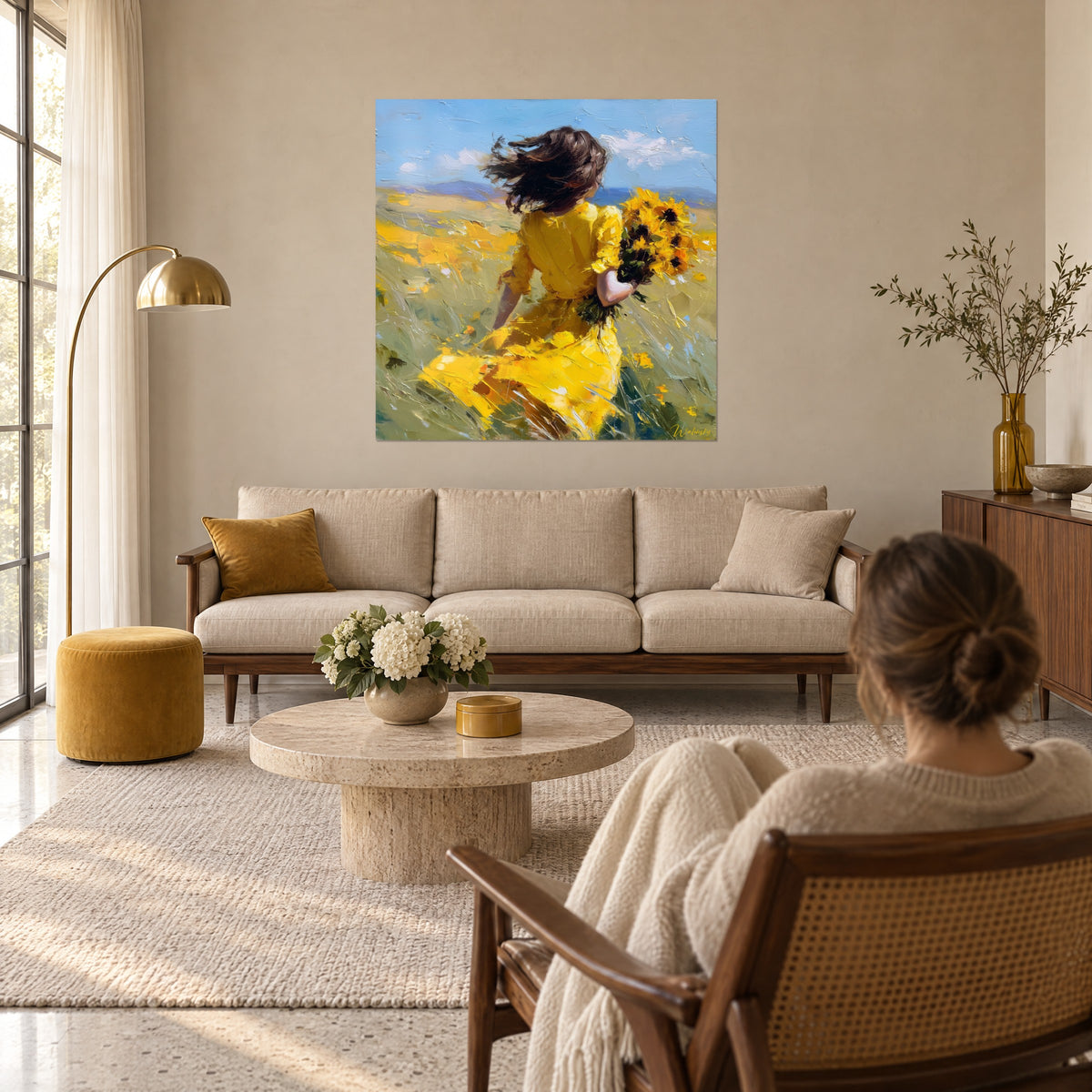 Schilderij jonge vrouw in een geel jurk die door een gouden veld rent, blauwe lucht, vrouw van achteren boven een bank in een lichte woonkamer