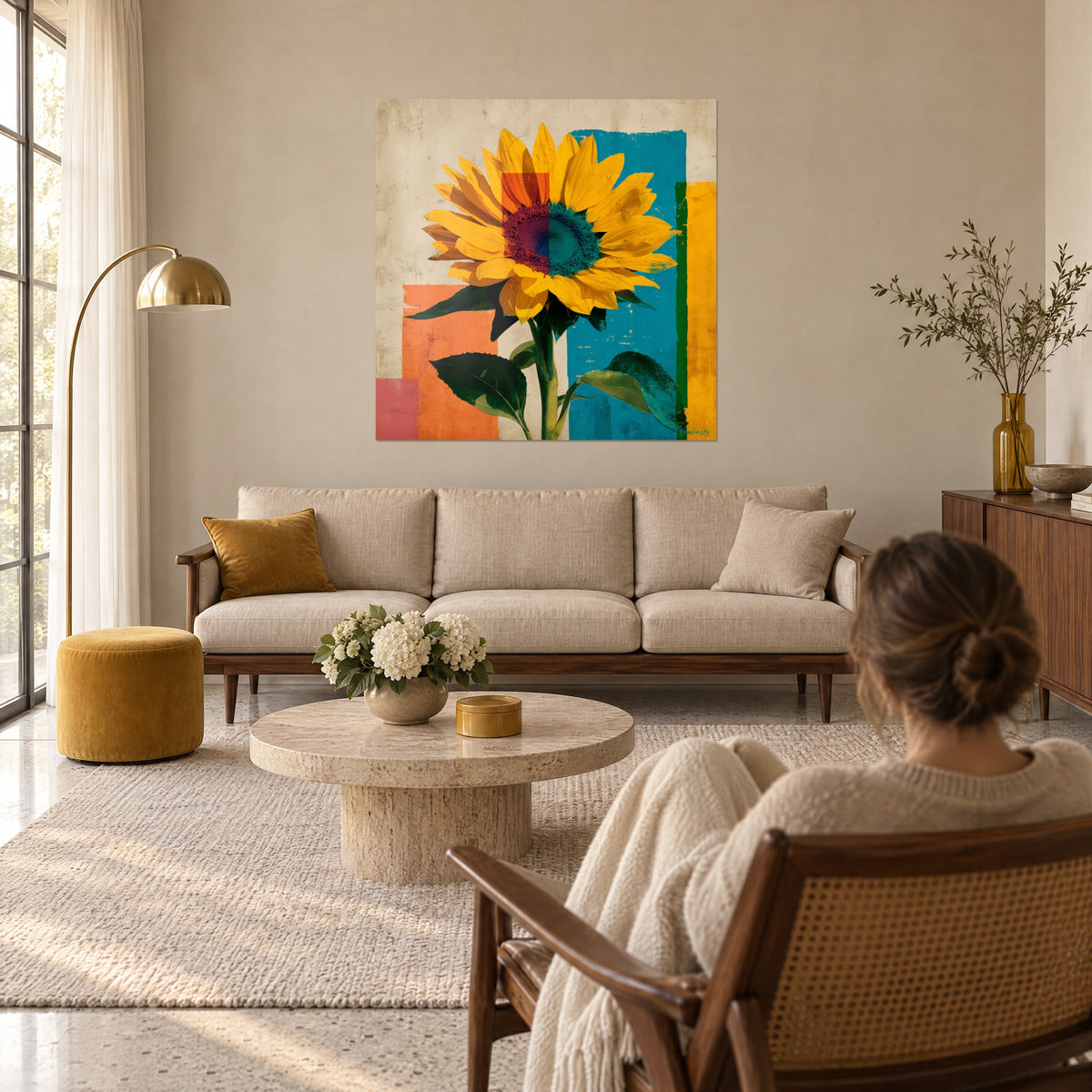 Tableau fleur de tournesol jaune safran sur aplats bleu canard et orange, vue d'une femme de dos, au-dessus d'un canapé dans un salon lumineux