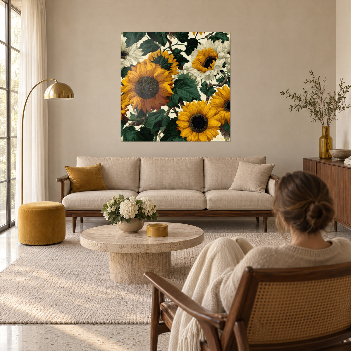 Wall art sunflowers with saffron-yellow petals and fir-green foliage, woman seen from behind, above a sofa in a bright living room