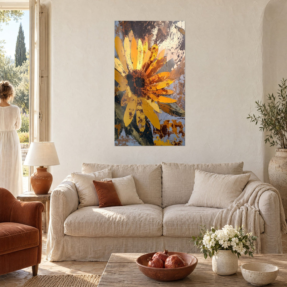 Cuadro girasol con pétalos amarillo azafrán salpicados de óxido, fondo marrón y gris, admirado por una mujer de espaldas sobre un sofá en un salón luminoso