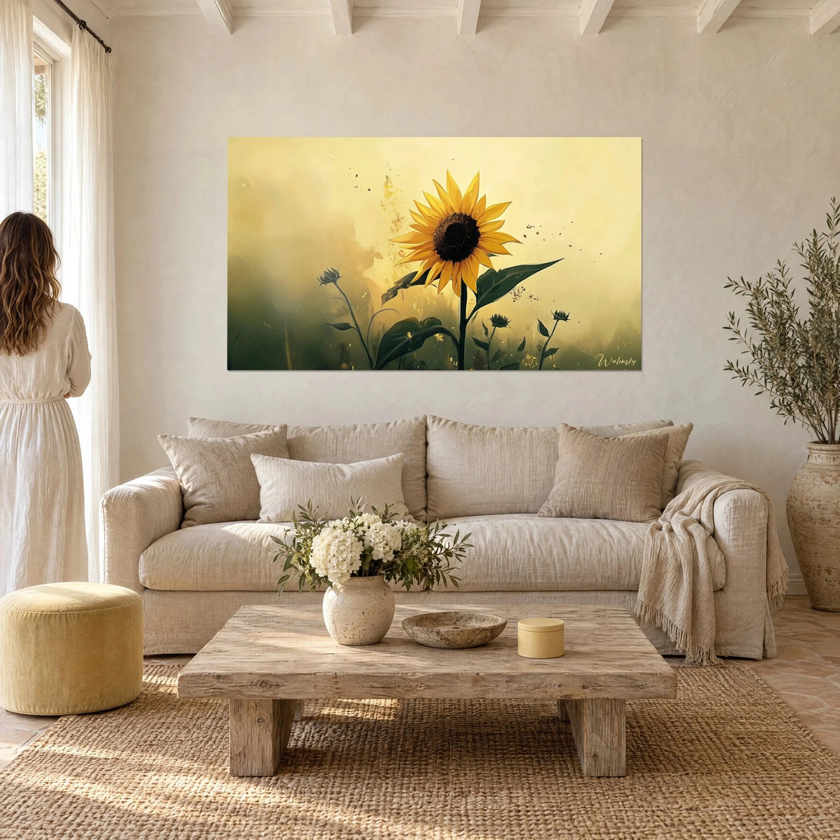 Cuadro girasol amarillo dorado con centro marrón, hojas verde oscuro sobre fondo crema, encima de un sofá en un salón luminoso
