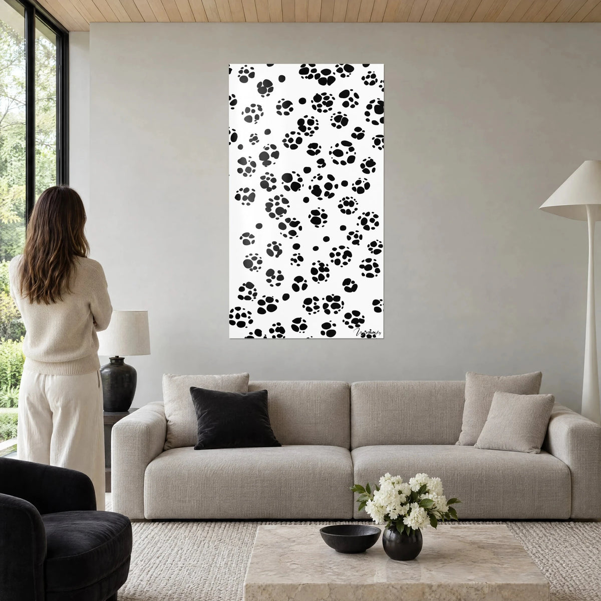 Tableau empreintes de pattes noires sur fond blanc, femme de dos, murs gris perle, au-dessus d'un canapé dans un salon lumineux