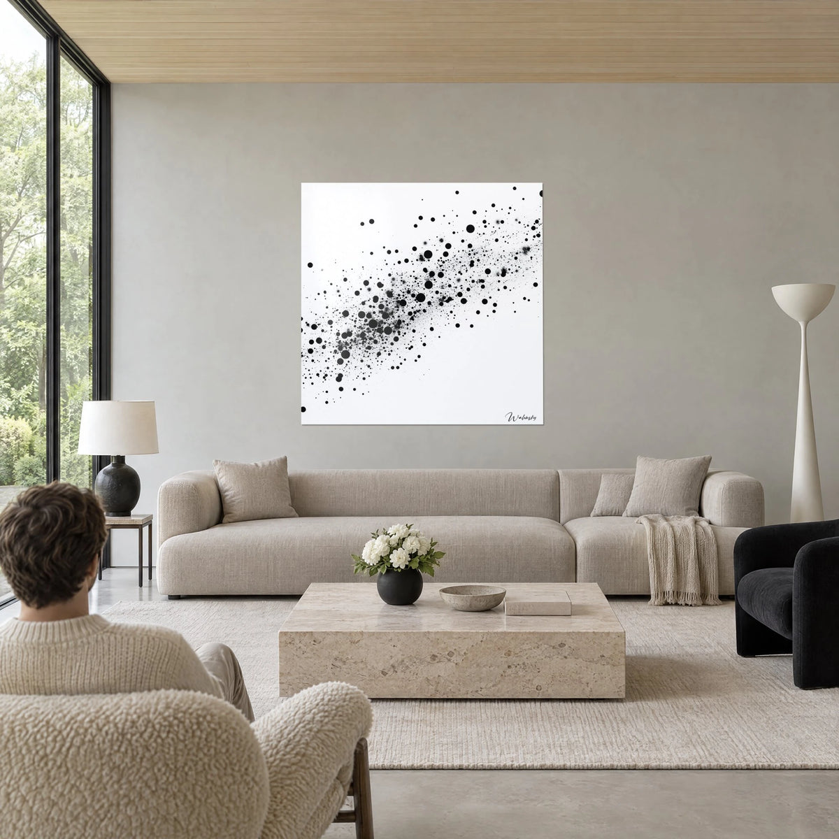 Wall art of a diagonal swarm of black ink dots on pure white background, two people seen from behind above a sofa in a bright living room