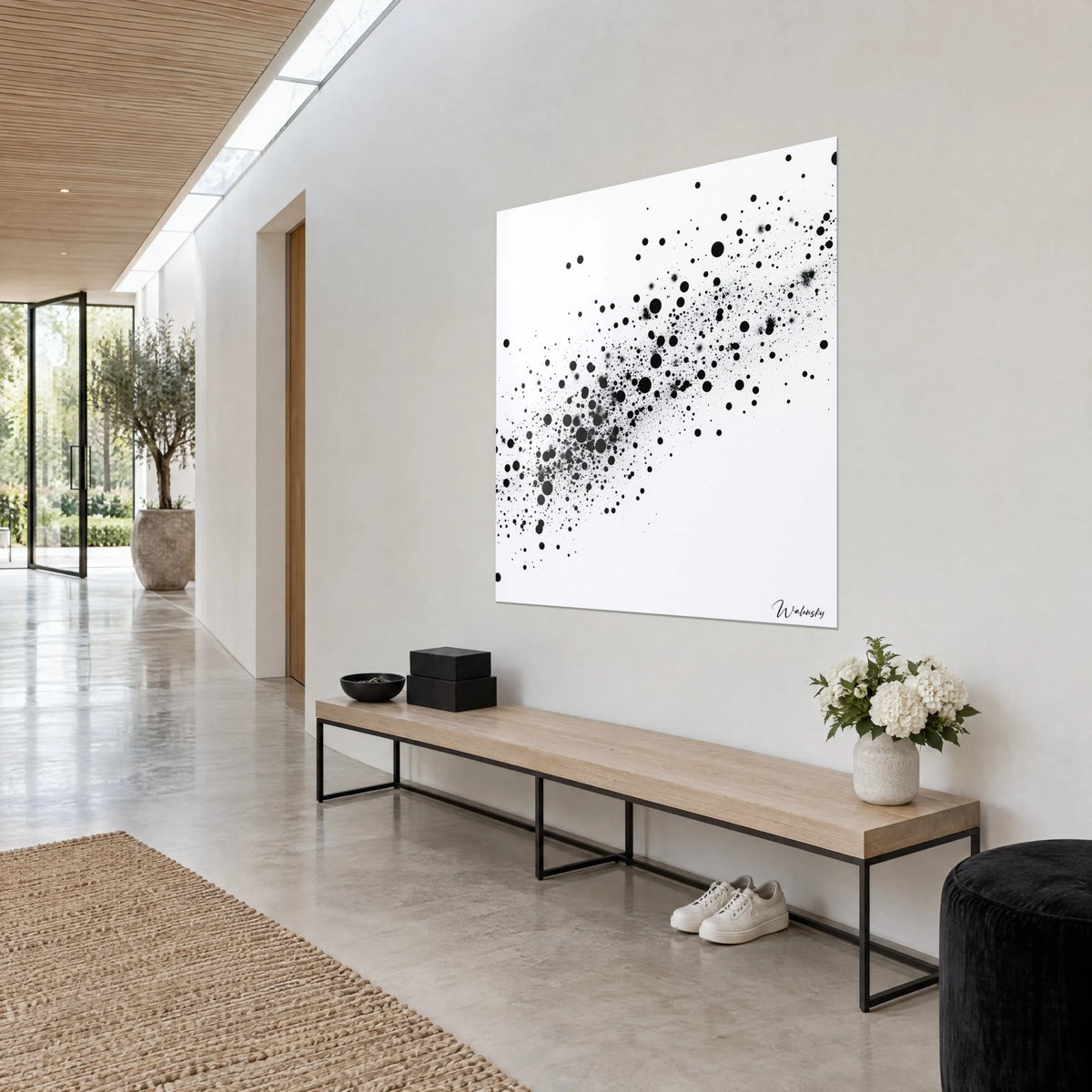 Wall art of a galaxy splattered with black specks and grey spray on white, three-quarter view, in a hallway of pale stone and wood