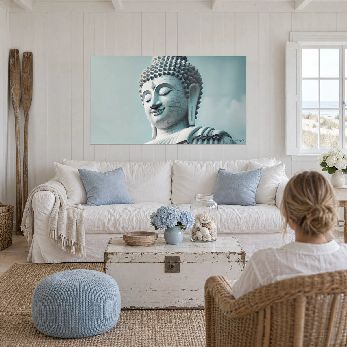 Quadro statua di Buddha in pietra con le palpebre chiuse, cielo grigio-azzurro e sorriso sereno, sopra un divano in un soggiorno luminoso