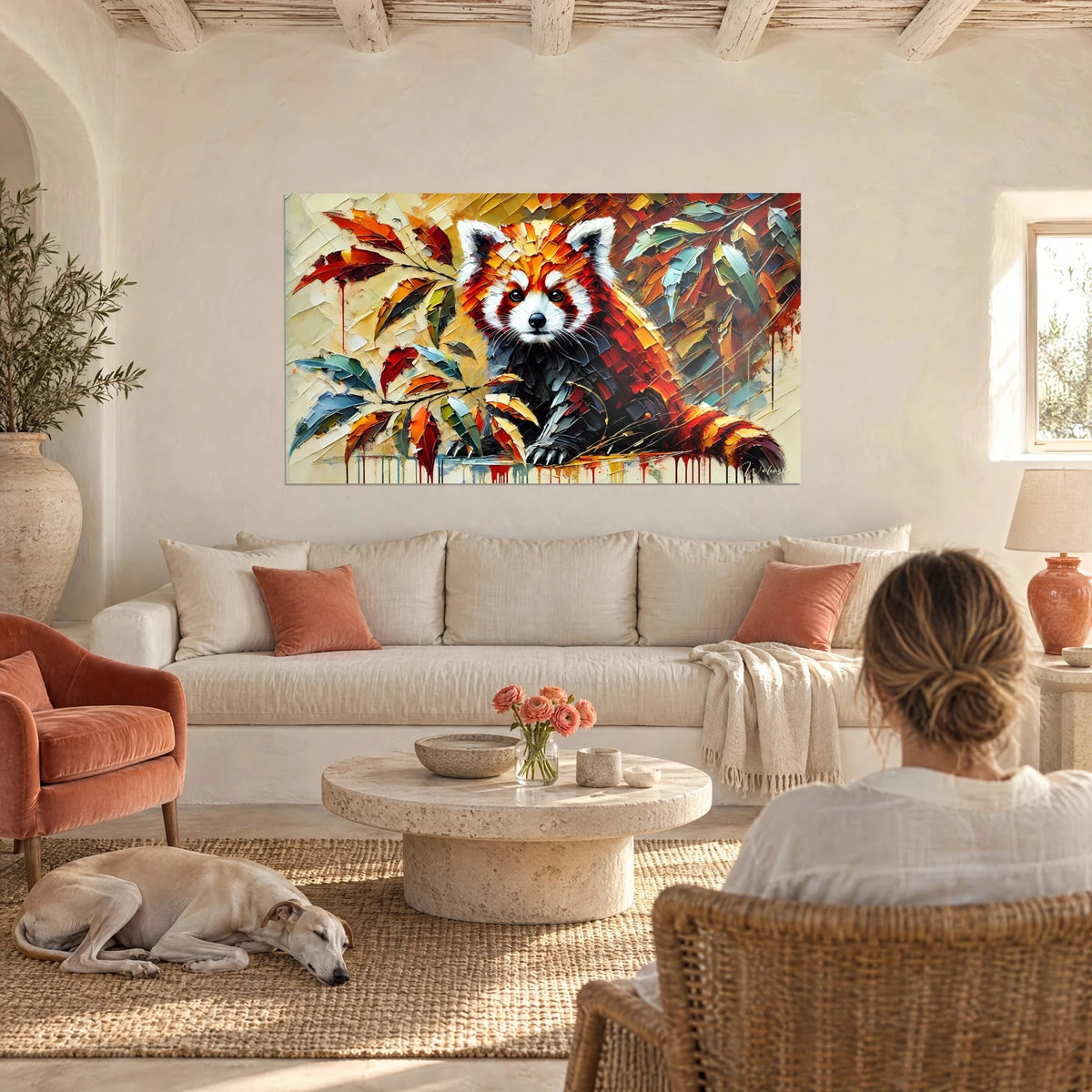 Quadro panda rosso dagli occhi neri e maschera bianca, foglie azzurrate e ruggine, una donna di spalle e un levriero, sopra un divano in un soggiorno luminoso