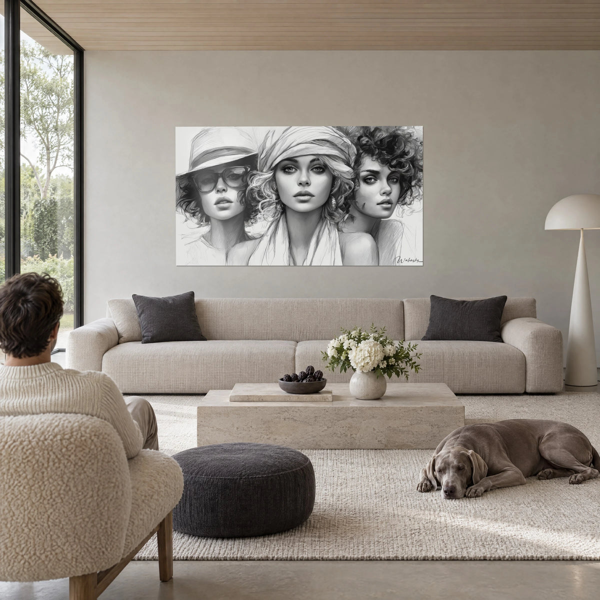 Cuadro de tres rostros femeninos en carboncillo blanco y negro, sombrero y gafas, una persona de espaldas, sobre un sofá en un salón luminoso
