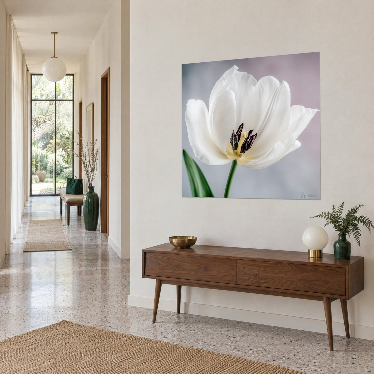 Tableau fleur blanche aux pétales soyeux et cœur jaune pâle piqueté de pourpre, au-dessus d'un buffet en bois dans un couloir