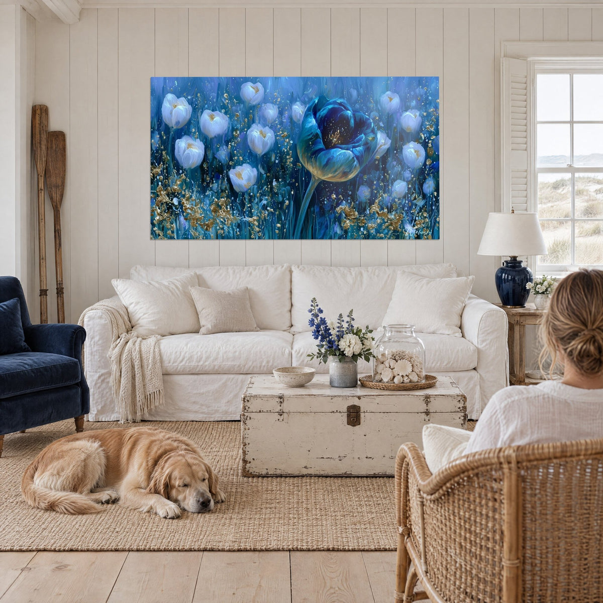 Gemälde einer riesigen blauen Tulpe, umgeben von weißen Blüten mit goldenen Glanzlichtern, eine Frau mit ihrem Retriever, über einem Sofa in einem hellen Wohnzimmer