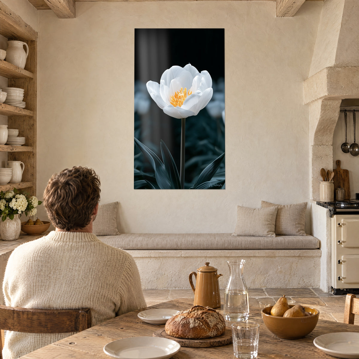 Tableau bouton de tulipe crème épanoui, étamines ambrées sur fond sombre, vu par un homme de dos attablé dans une cuisine en pierre
