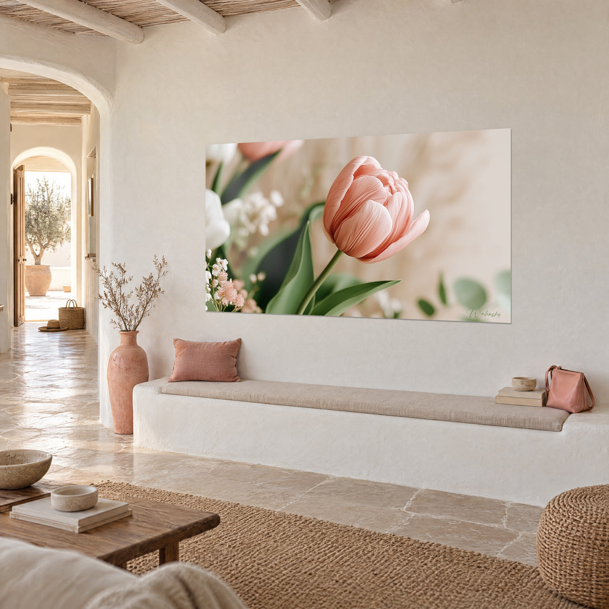 Quadro con un fiore sbocciato rosa pallido e stelo verde tra rami di eucalipto, appeso di tre quarti su una parete di calce bianca