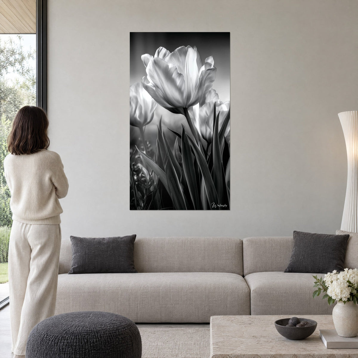 Schilderij witte tulp in zwart-wit, parelgrijze bloembladen op een donkere achtergrond, boven een bank in een lichte woonkamer