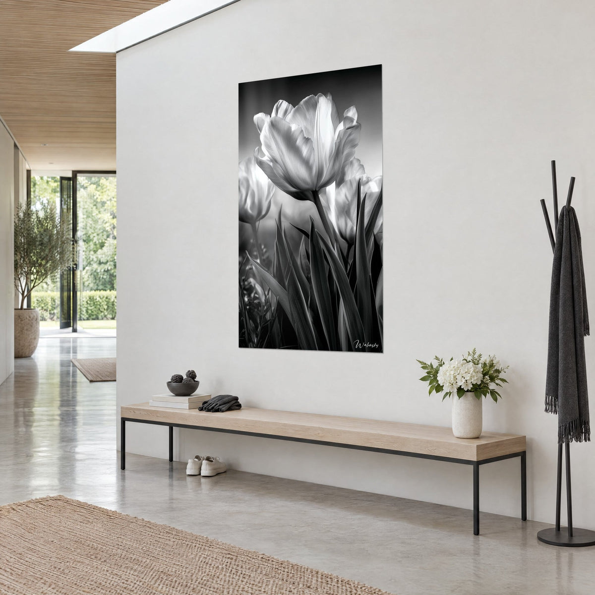 Schilderij ivoorkleurige tulpenbloem met zilveren nerven, slanke zwarte bladeren, opgehangen boven een bank van licht hout