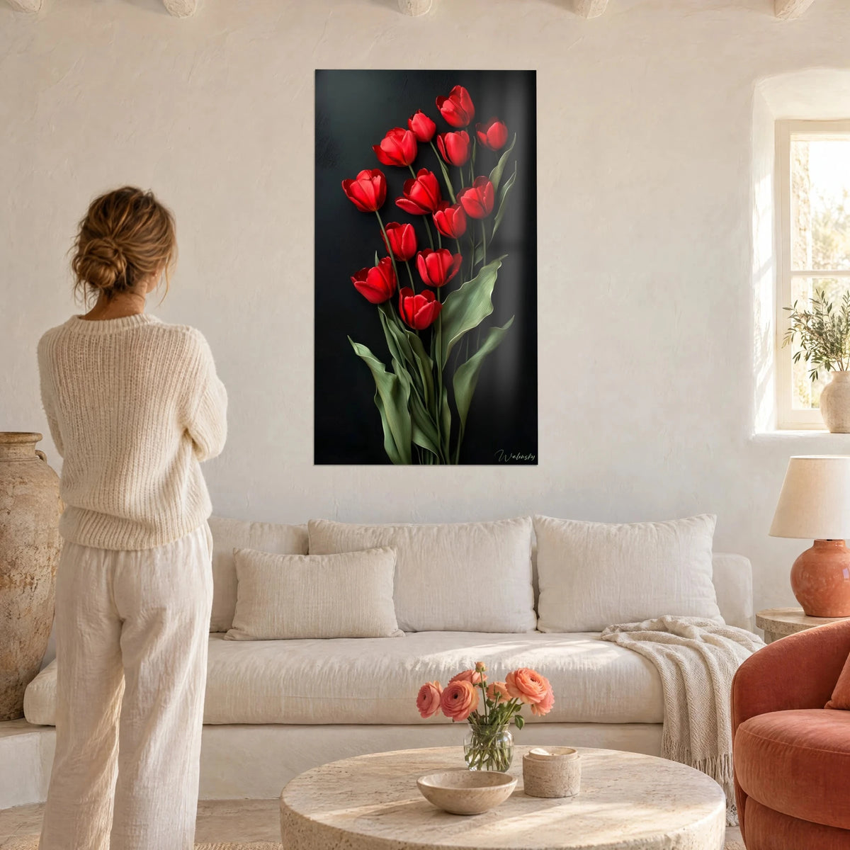 Schilderij boeket felrode tulpen op een zwarte achtergrond, saliegroene bladeren, opgehangen boven een bank waarop een vrouw met de rug naar de kijker zit in een lichte woonkamer