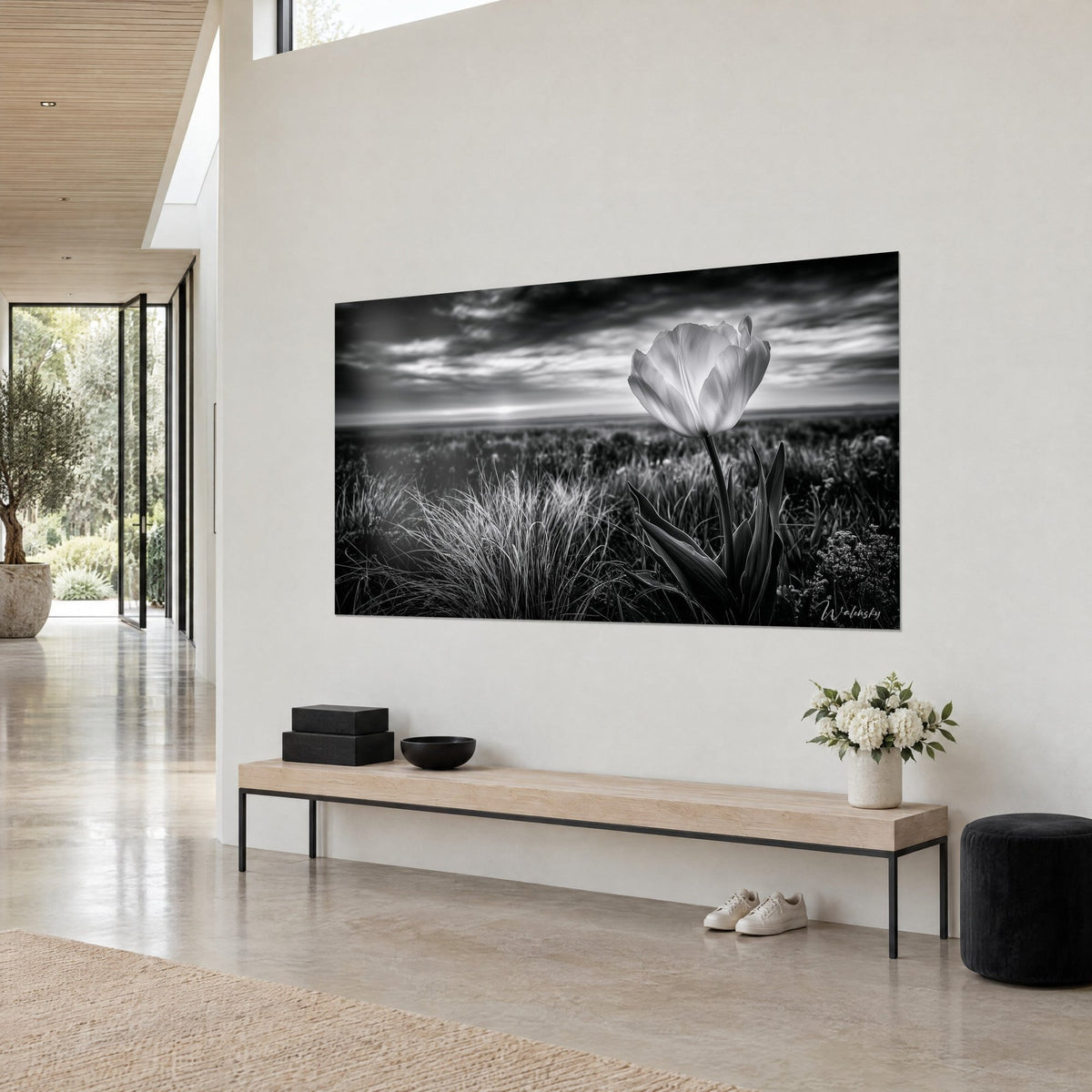 Tableau fleur immaculée aux pétales nacrés dressée dans des herbes grises, ciel sombre et soleil pâle, au-dessus d'un banc en bois
