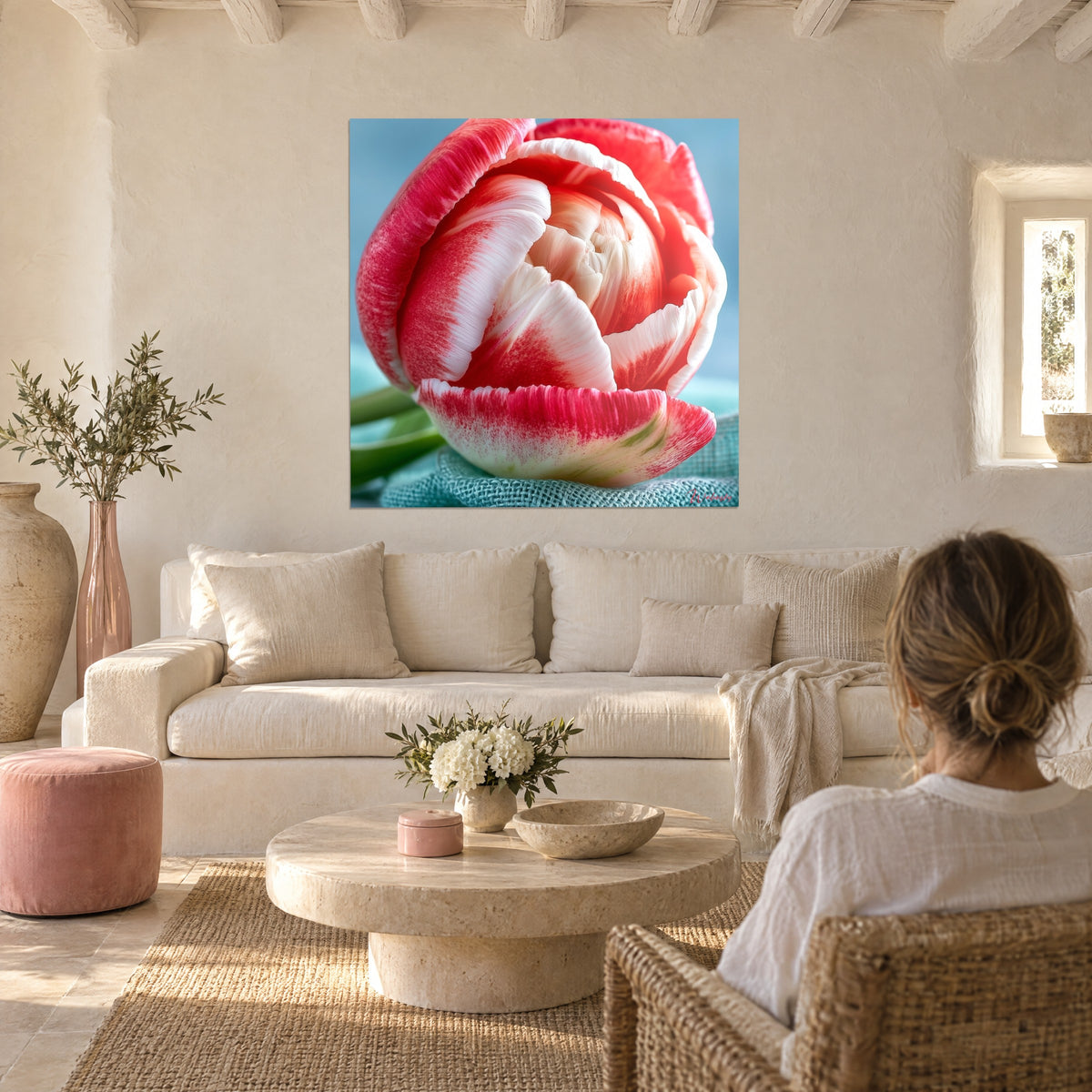 Wall art pink and white tulip with a spiral of velvety petals on a sky-blue background, woman seen from behind, above a sofa in a bright living room