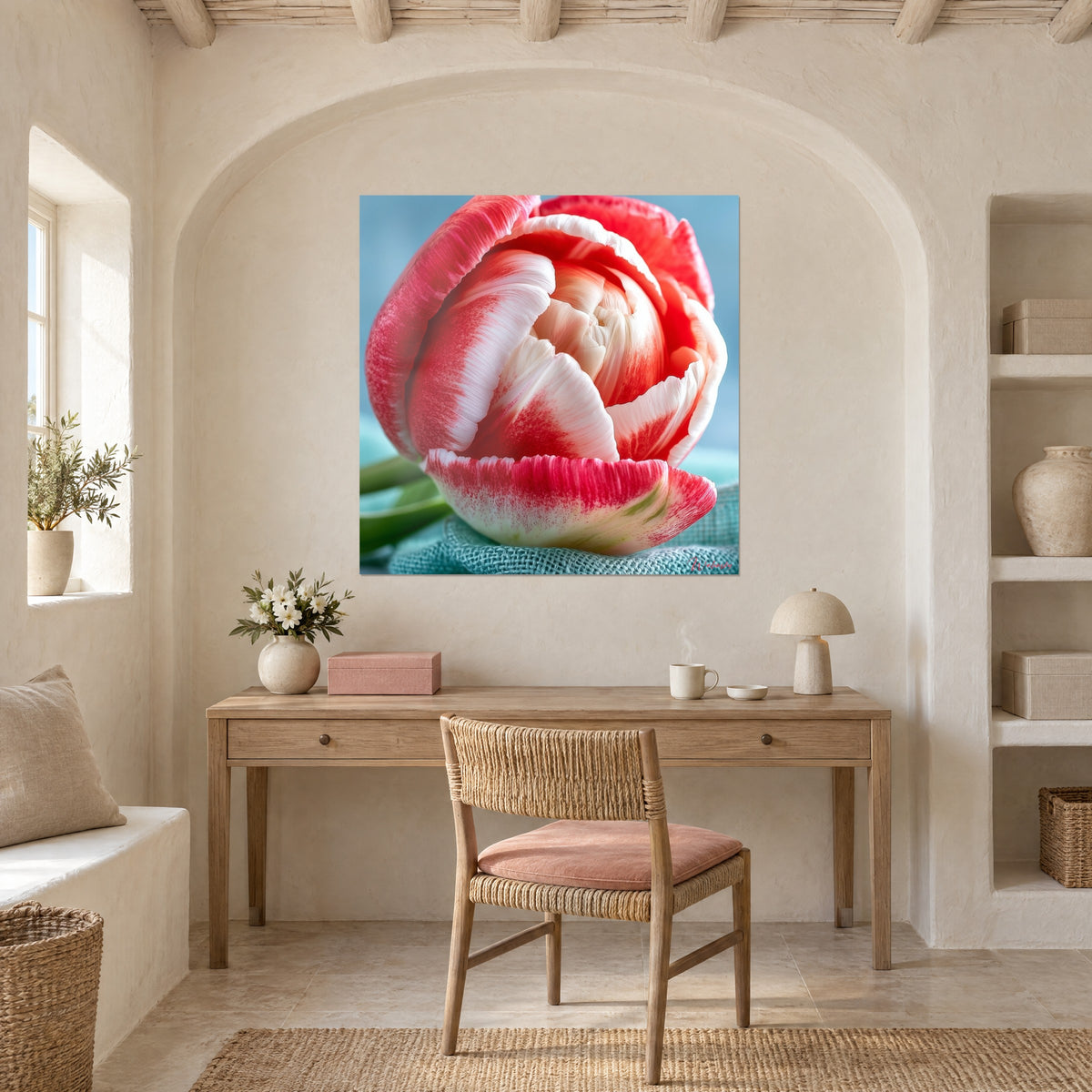 Wall art velvety cherry-red and pearlescent white petals, green stem, on a cream wall above a wooden desk and a rattan chair