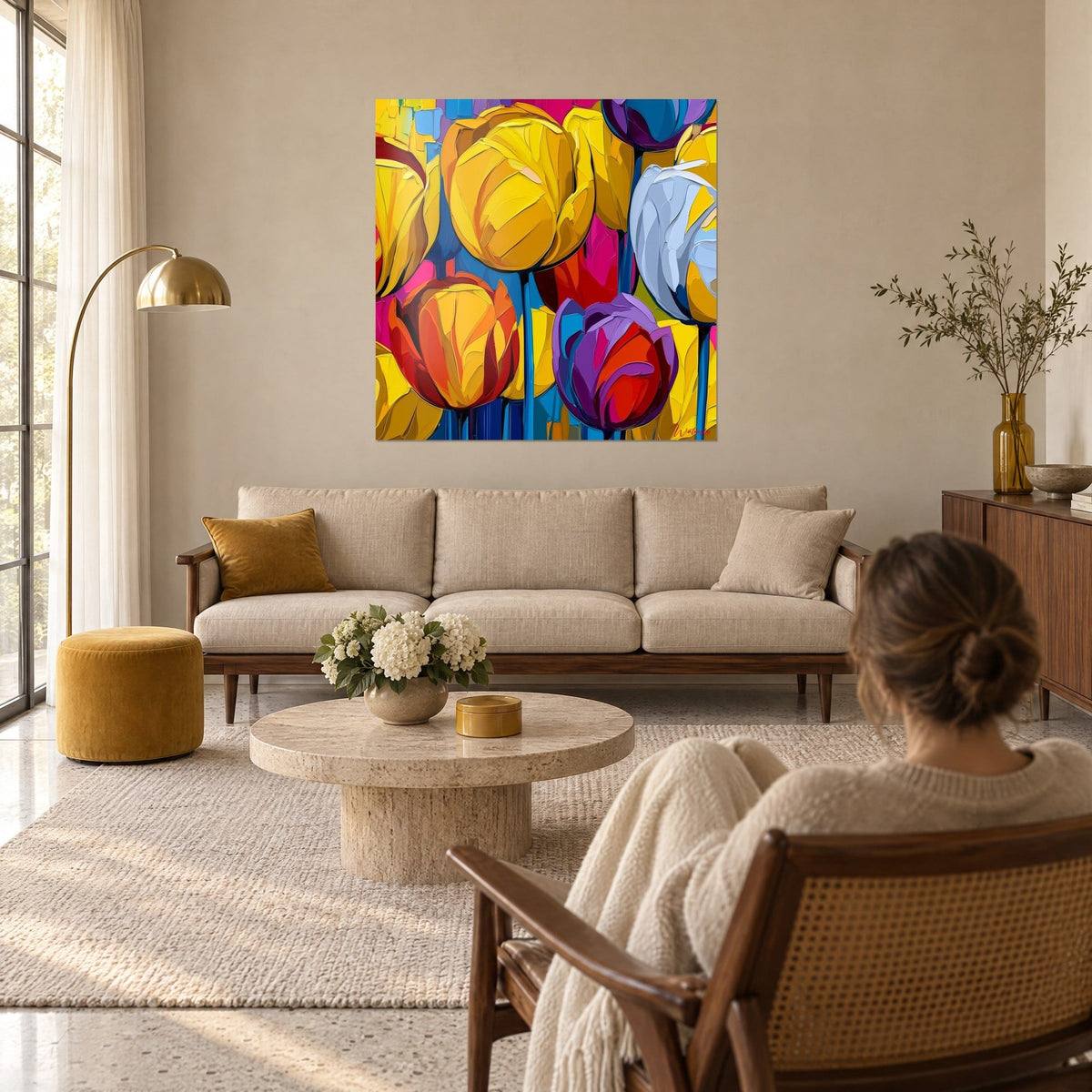 Wall art tulip bouquet in sunny yellow and fuchsia pink, thick palette-knife strokes, woman seen from behind, above a sofa in a bright living room