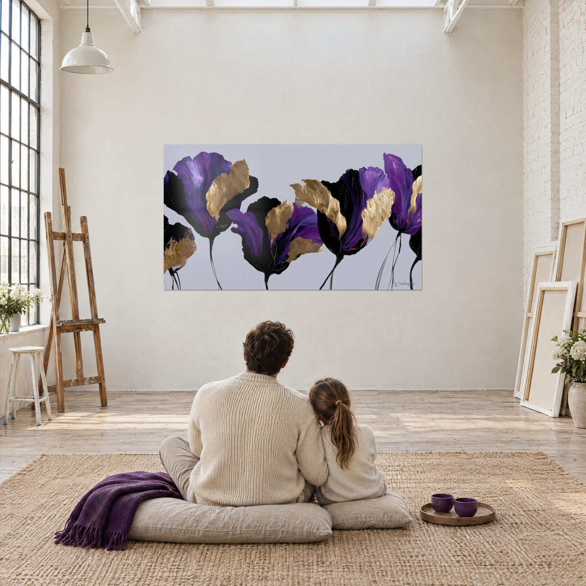 Wall art of purple gold-touched tulips on pearl grey background, facing an adult and a child seated back to back on a cushion in an artist's loft