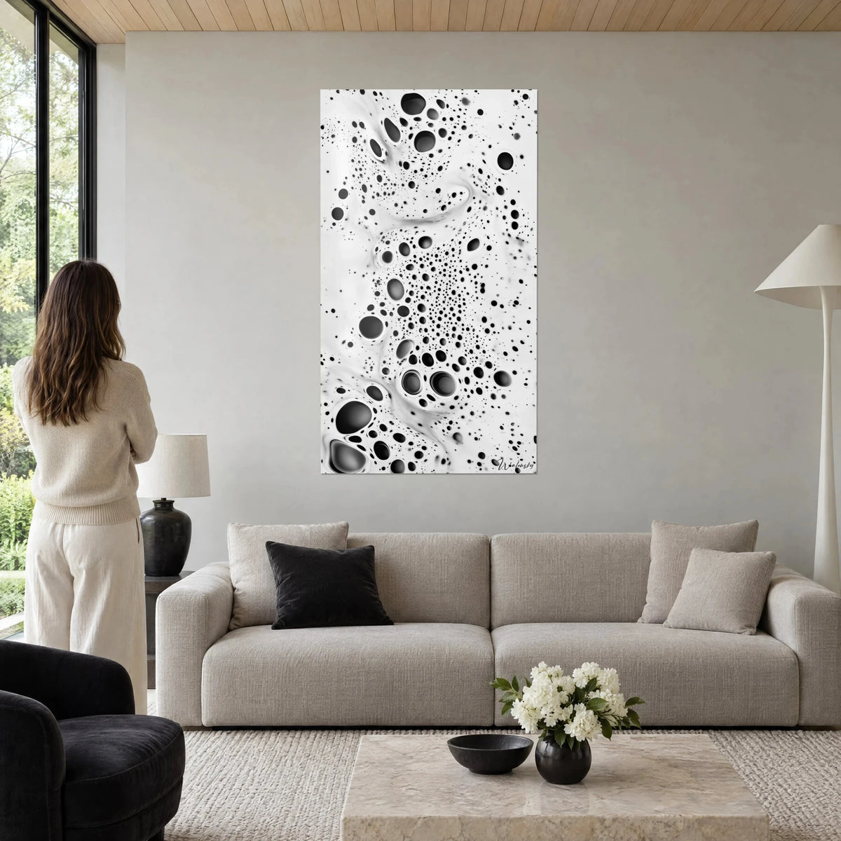 Tableau bulles noires en tourbillon sur fond blanc crème, femme de dos, au-dessus d'un canapé dans un salon lumineux