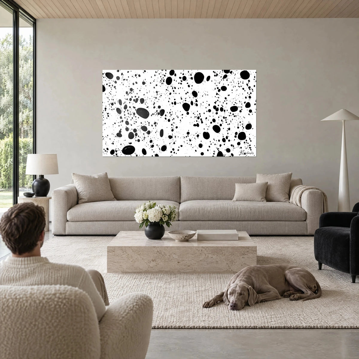 Cuadro de manchas de tinta negra salpicadas sobre fondo blanco, un Weimaraner tumbado encima de un sofá en un salón luminoso