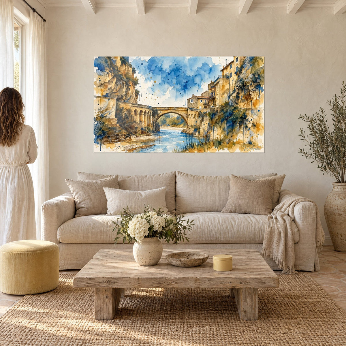 Gemälde Steinbrücke in Ockertönen über einem blauen Fluss, indigoblauer Aquarellhimmel, Frau von hinten, über einem Sofa in einem hellen Wohnzimmer