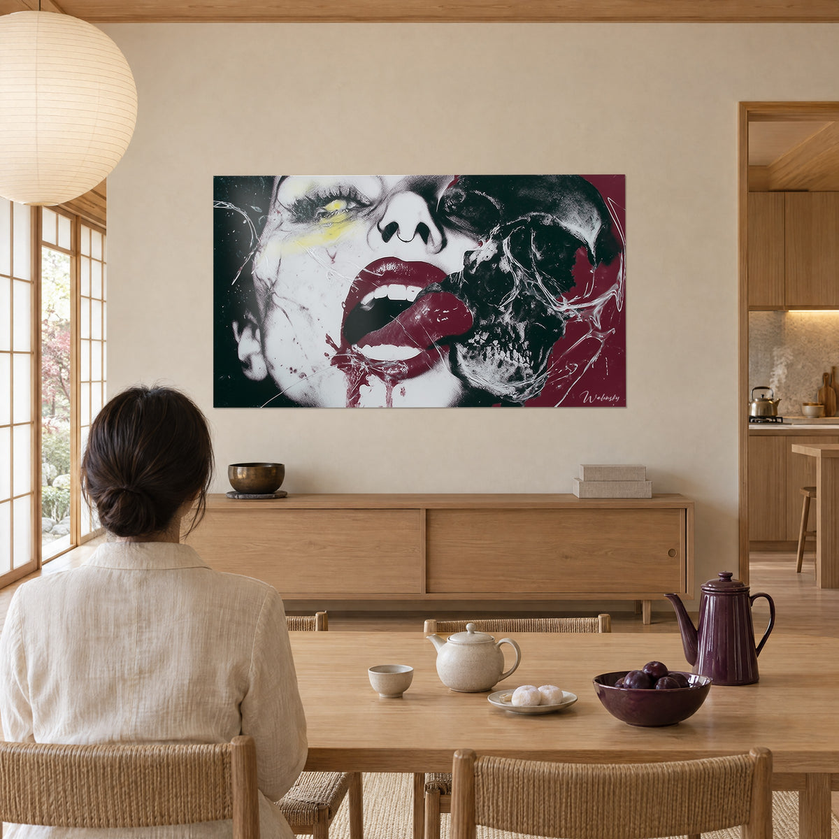 Cuadro de mujer de rostro pálido y calavera partida, labios rojo vino, regueros grises, visto de espaldas desde una mesa de madera clara, comedor de estilo japandi