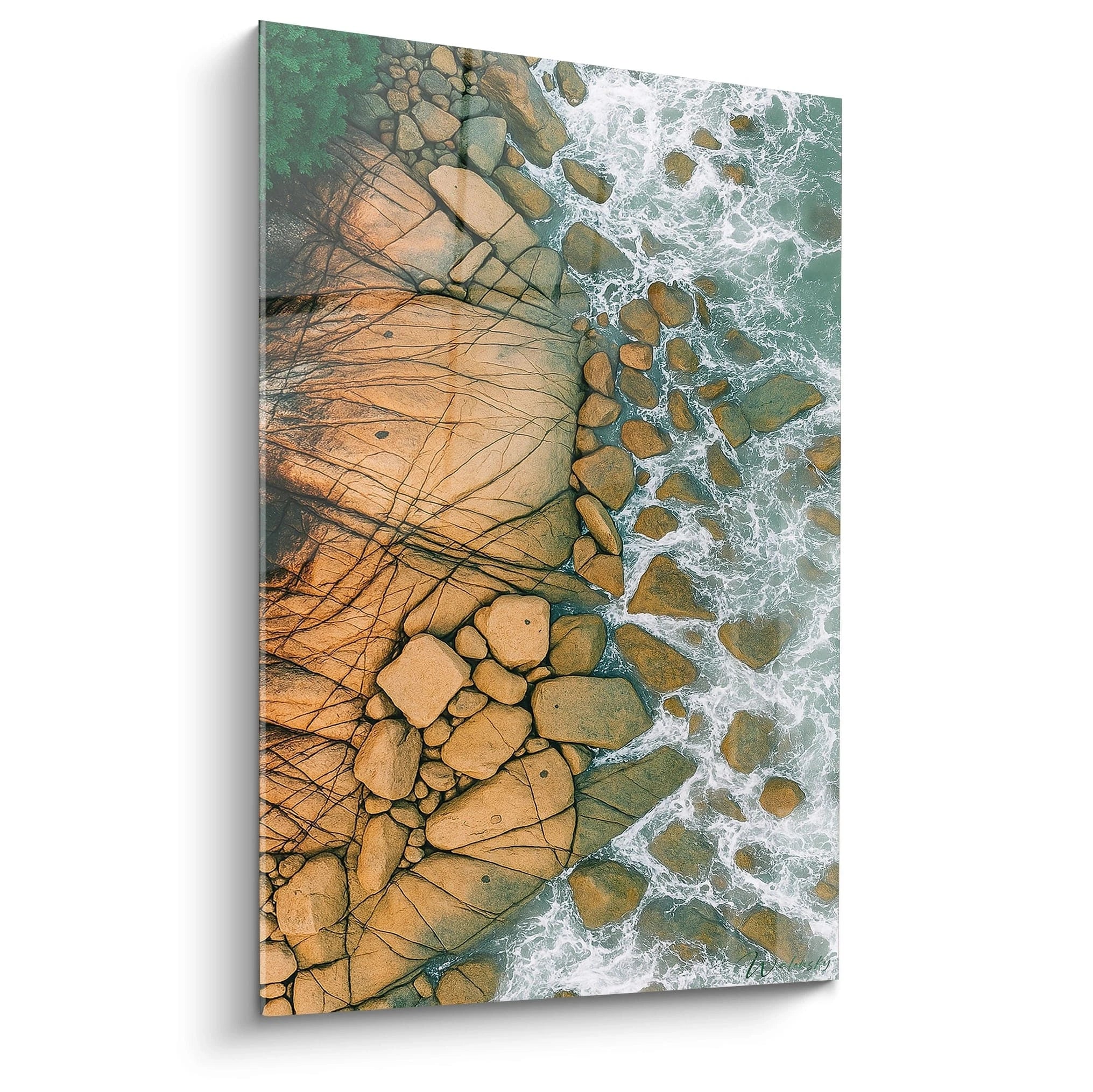 Un tableau vue aérienne présentant la rencontre entre falaise rocheuse beige et mer turquoise, avec des rochers épars et végétation verte. Les textures naturelles des pierres fissurées contrastent avec l'écume blanche des vagues.
