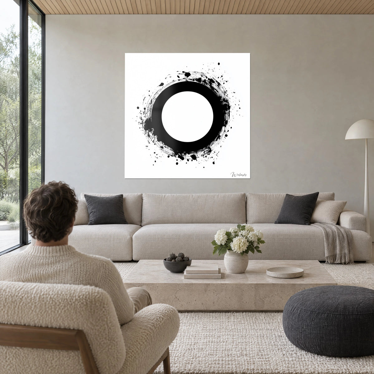 Cuadro círculo zen de tinta negra salpicada sobre fondo blanco, hombre de espaldas, sobre un sofá en un salón luminoso