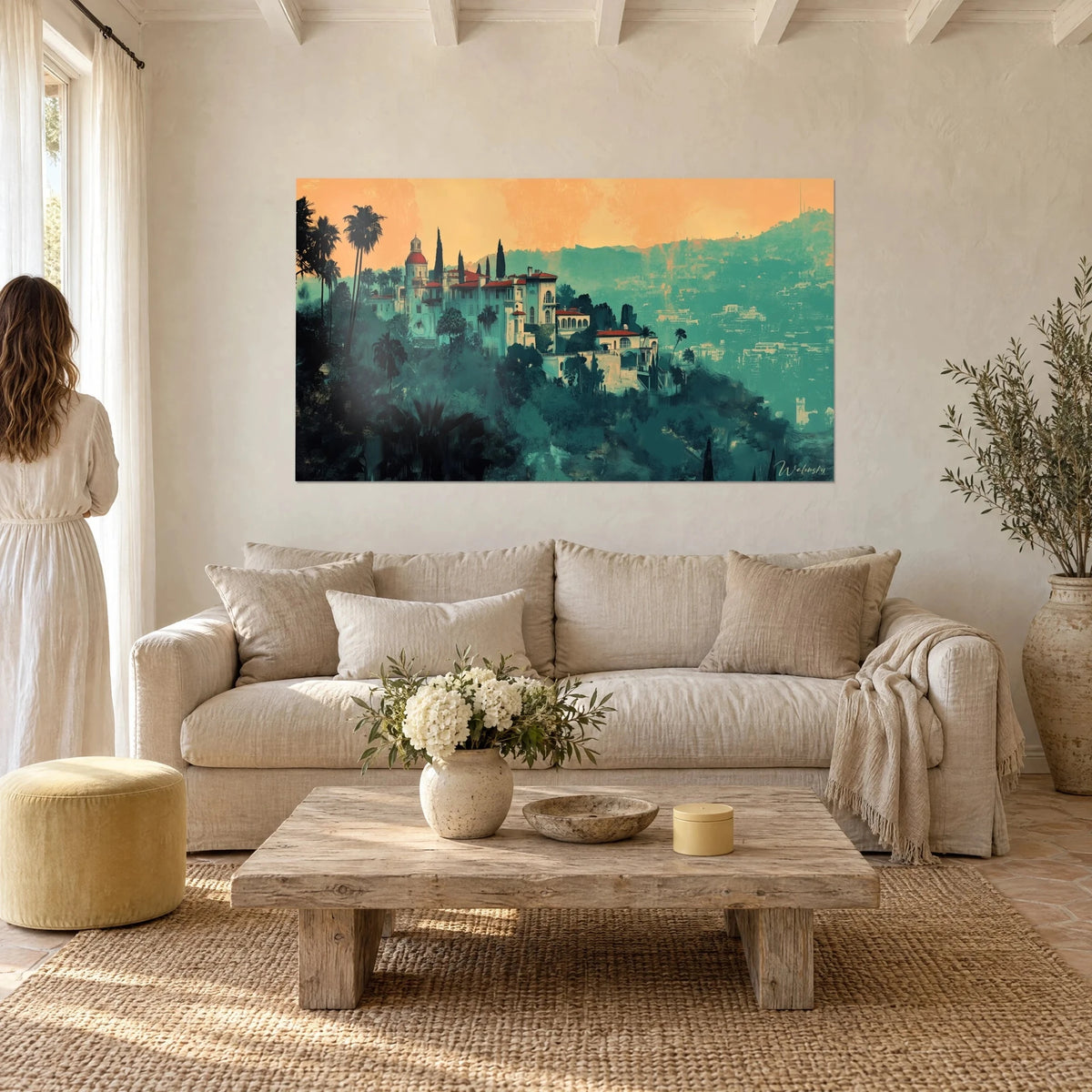 Gemälde italienische Villa mit roten Dächern auf türkisfarbenem Hügel, orangefarbener Himmel, Rückansicht eines Paares über einem Sofa in einem hellen Wohnzimmer