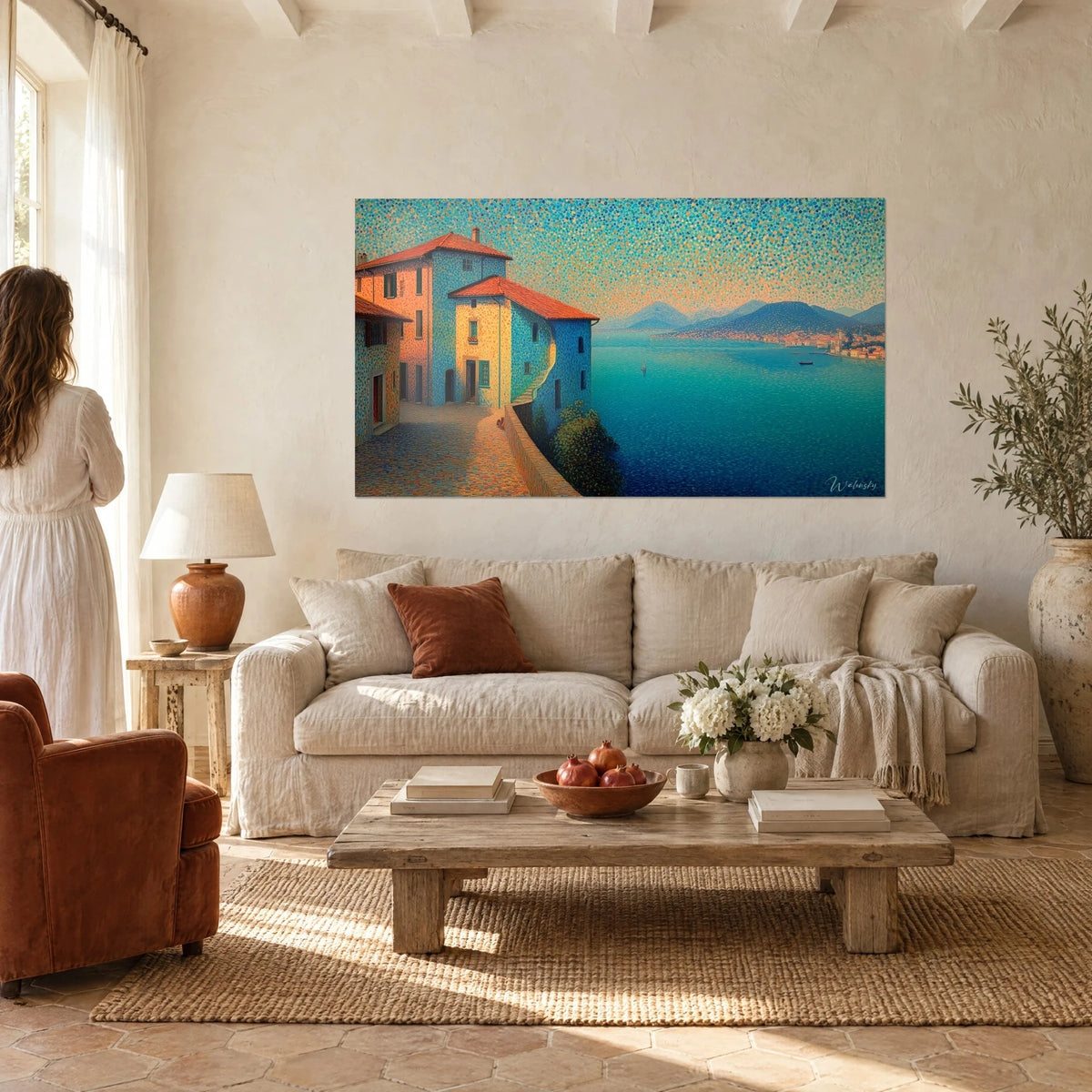 Tableau village pointilliste aux façades bleues et ocre, lac turquoise et montagnes, au-dessus d'un canapé dans un salon lumineux