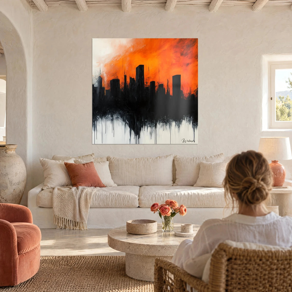 Schilderij van zwarte wolkenkrabbers tegen een fel oranje en crèmewitte lucht, gezien door een vrouw van achteren, boven een bank in een lichte woonkamer