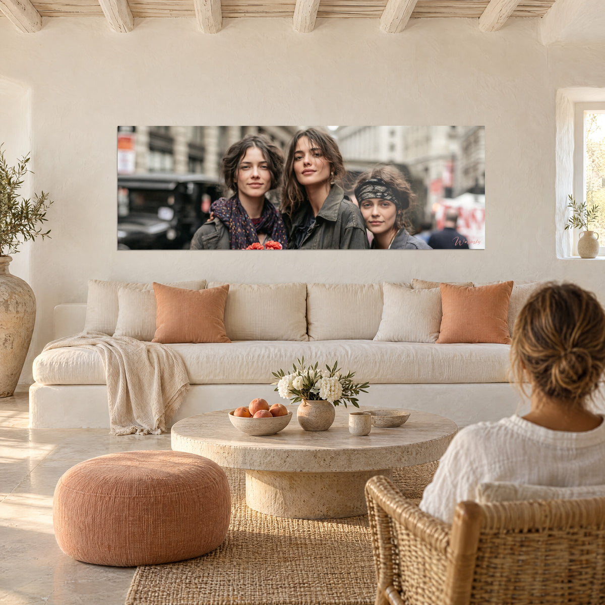 Wall art three brunette friends huddled together in the street, plum scarf and red flowers, hanging above a sofa in a bright living room