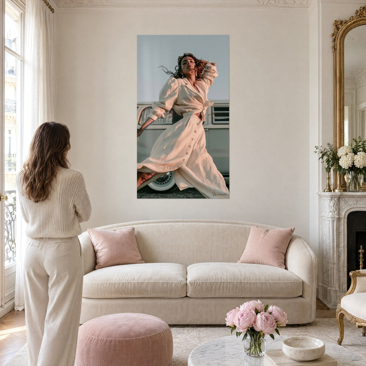 Wall art of a young woman in an ivory dress leaping, brown hair blowing in the wind, cream camper van, above a sofa in a bright living room