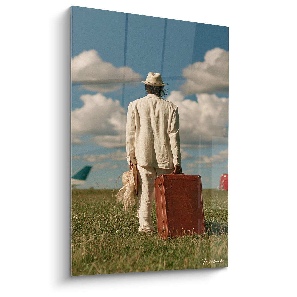 Voyageur en costume ivoire portant une valise terracotta dans un champ vert sous un ciel bleu nuageux