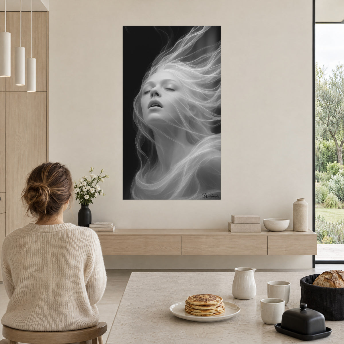 Cuadro figura femenina envuelta en una nube de cabello plateado y de ébano, frente al rincón de comedor de una cocina abierta a la naturaleza