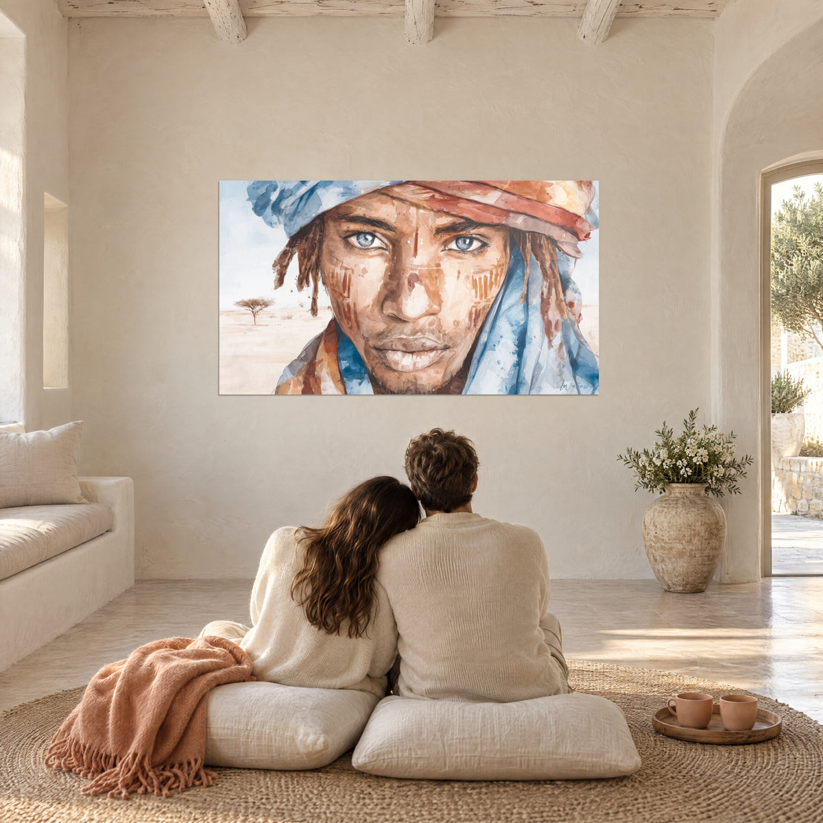 Tableau touareg au regard glacé, turban bleu et rouge brique, face à un couple de dos assis sur des coussins crème