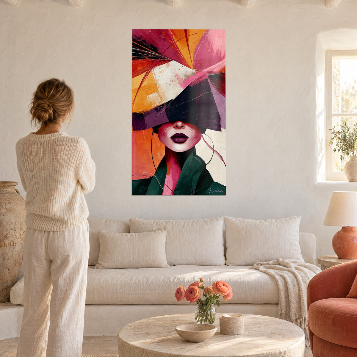 Schilderij van een vrouwengezicht onder een geometrische pruimkleurige hoed, aubergine lippen, oranje en roze achtergrond, vrouw van achteren, boven een bank in een lichte woonkamer