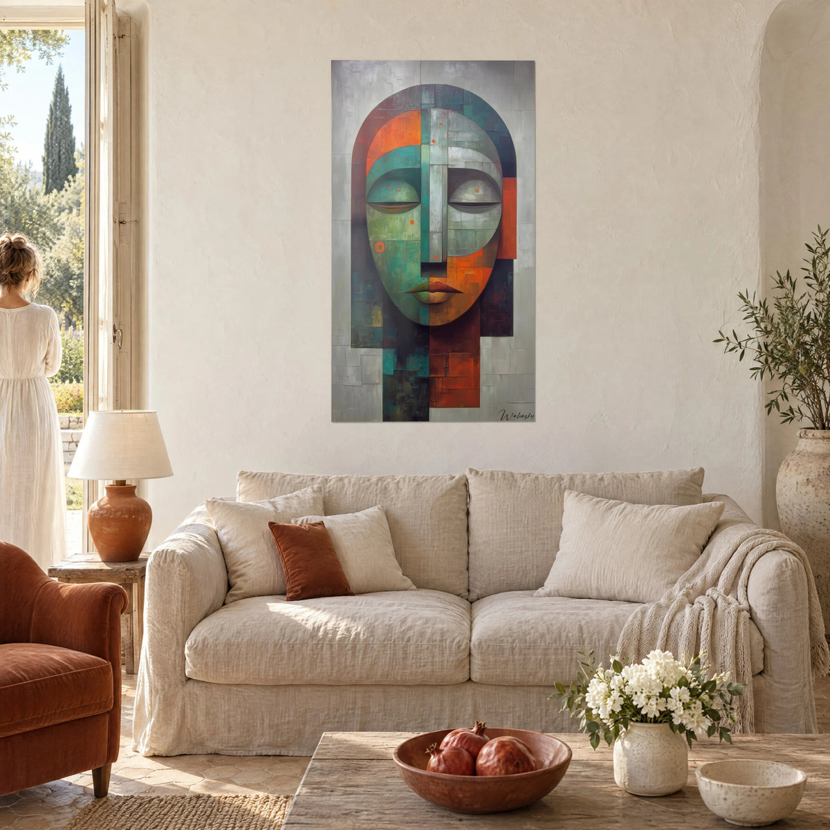 Gemälde einer stilisierten Maske mit geschlossenen Augen, halb graugrün und halb gebranntes Orange, eine Frau von hinten, über einem Sofa in einem hellen Wohnzimmer