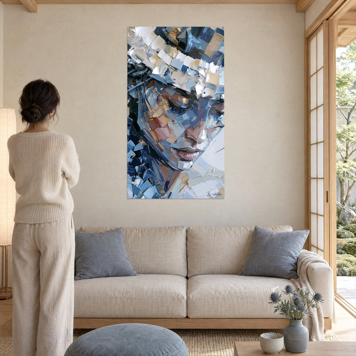 Quadro volto inclinato in frammenti blu notte e bianco crema, ciglia nere arricciate, sopra un divano in un soggiorno luminoso