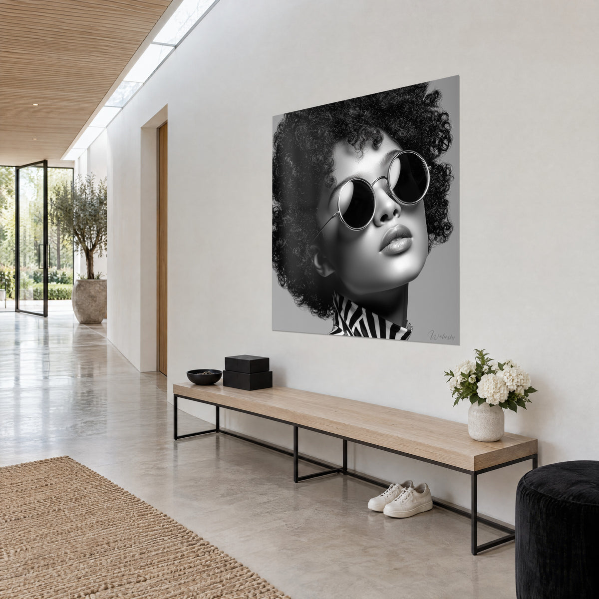 Cuadro joven de cabello rizado, barbilla levantada, lentes redondos negros y gris perla, sobre una pared blanca de pasillo en tres cuartos