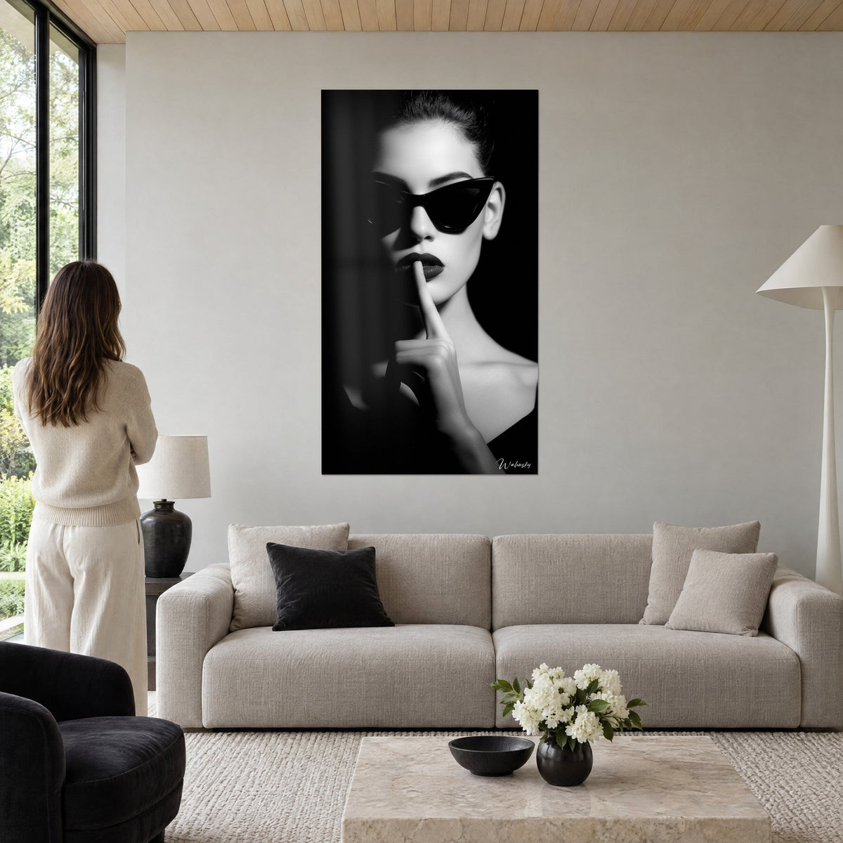 Gemälde Frau mit schwarzer Schmetterlingsbrille, Finger auf den Lippen, elfenbeinfarbene Haut auf schwarzem Hintergrund, über einem Sofa in einem hellen Wohnzimmer