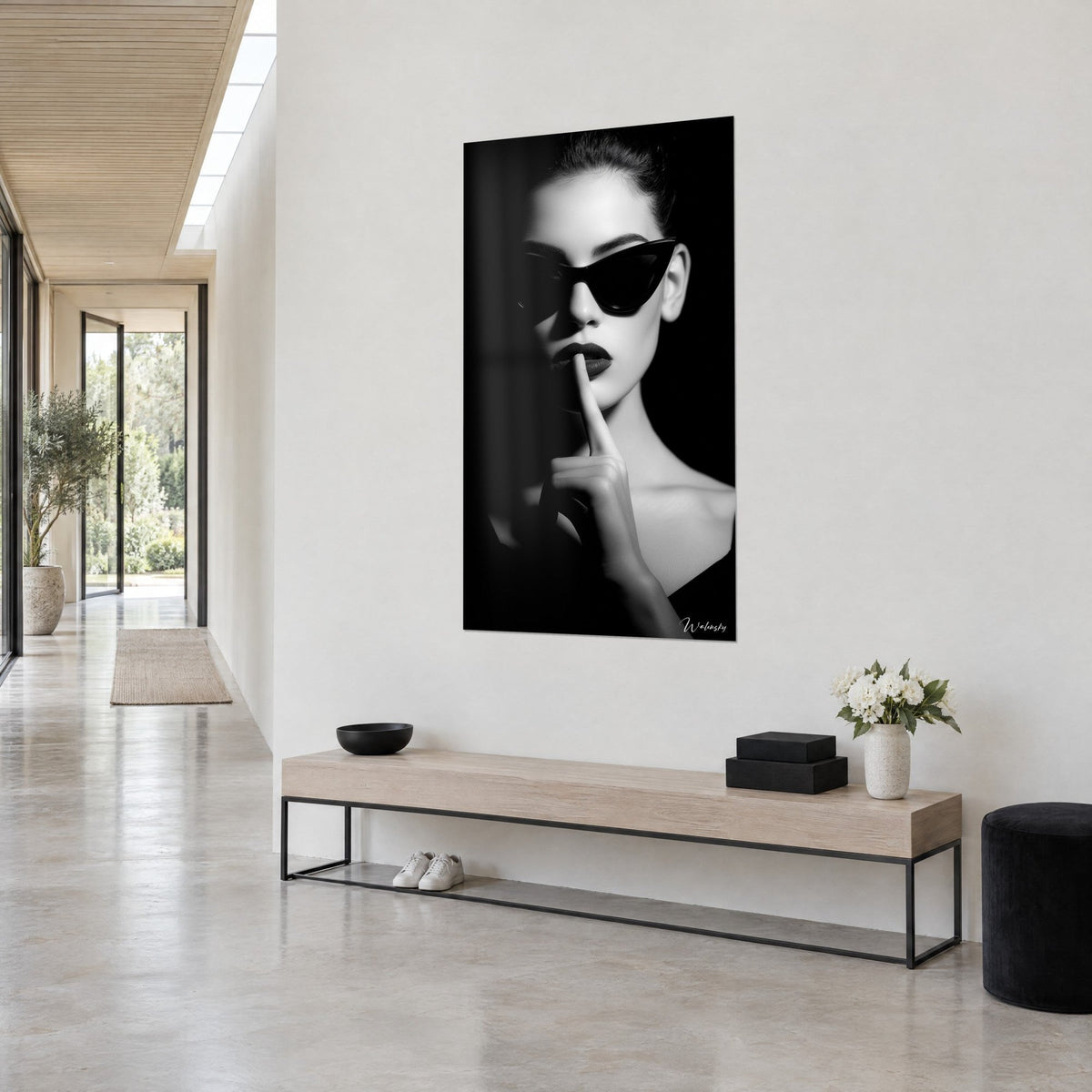 Cuadro retrato en claroscuro, labios oscuros, índice levantado, moño suelto y hombros pálidos sobre negro profundo, pared blanca y pasillo acristalado