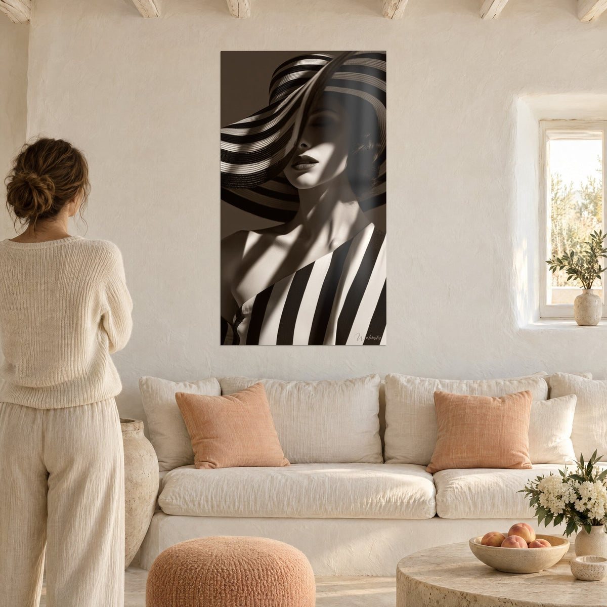 Tableau femme au chapeau rayé noir et crème, lèvres sépia, regarde par une femme de dos, au-dessus d'un canapé dans un salon lumineux