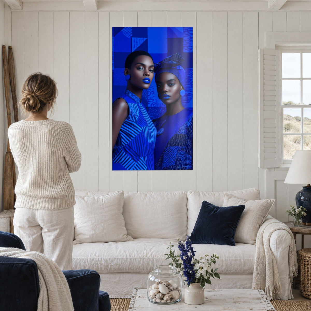 Schilderij duo van modellen in elektrisch blauw, kobaltblauwe lippen en gestreepte jurk, van achteren gezien boven een bank in een lichte woonkamer