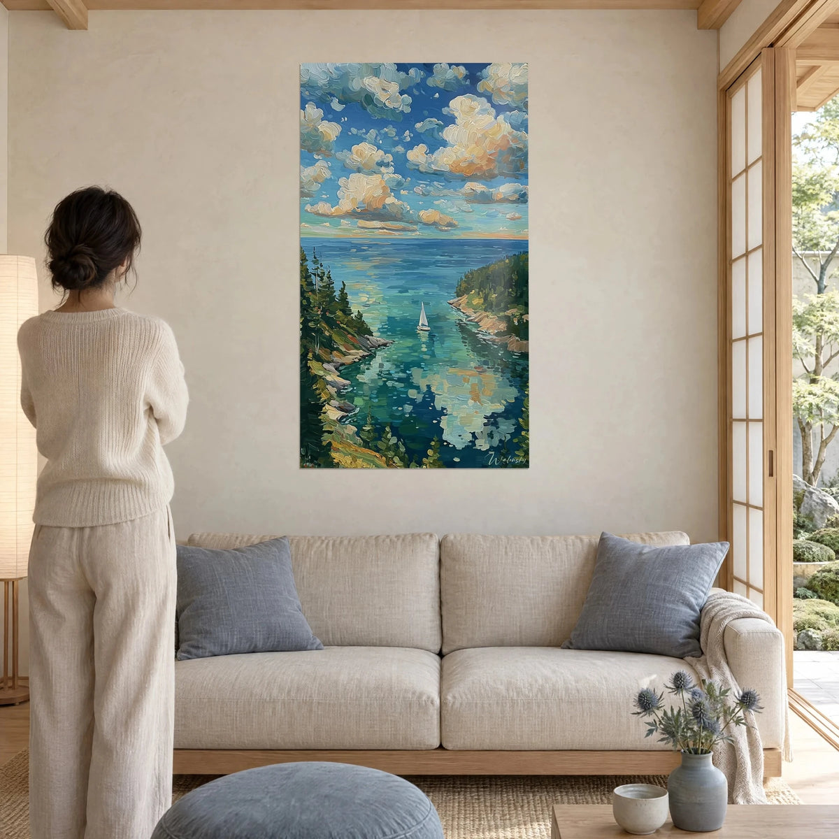 Tableau voilier blanc sur crique turquoise, nuages crème et ocre, femme de dos, au-dessus d'un canapé dans un salon lumineux