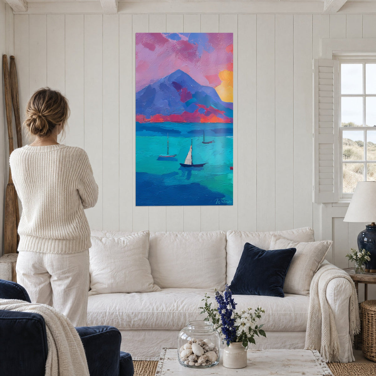 Schilderij blauwgrijze berg onder roze wolken, zeilboten op turquoise water, boven een bank in een lichte woonkamer
